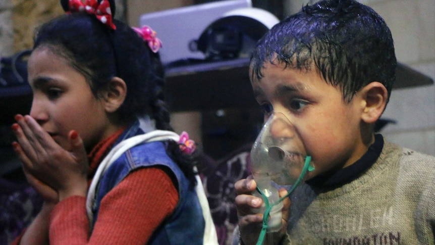 A small boy receives oxygen through a respirator with a small girl sitting next to him.