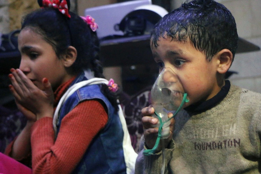 A small boy receives oxygen through a respirator with a small girl sitting next to him.