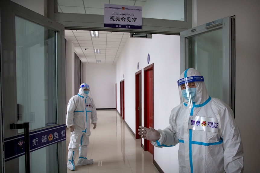 Security officers in protective suits stand in a hallway with rooms for video meetings