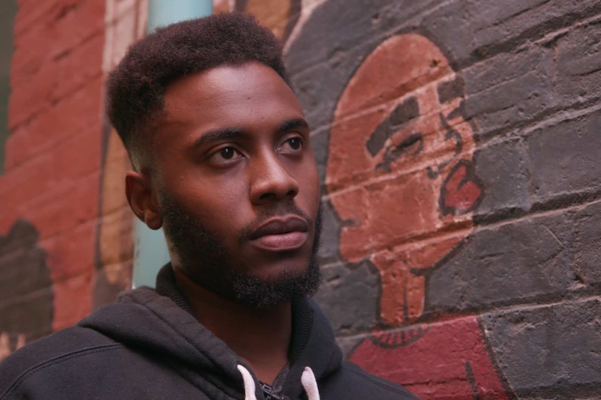 Jamali Musa stands in front of a wall covered in graffiti