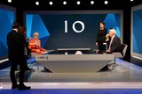 Theresa May wears and orange suit, which is adjusted by on-set assistants as jeremy paxman sits across from her sipping a coffee