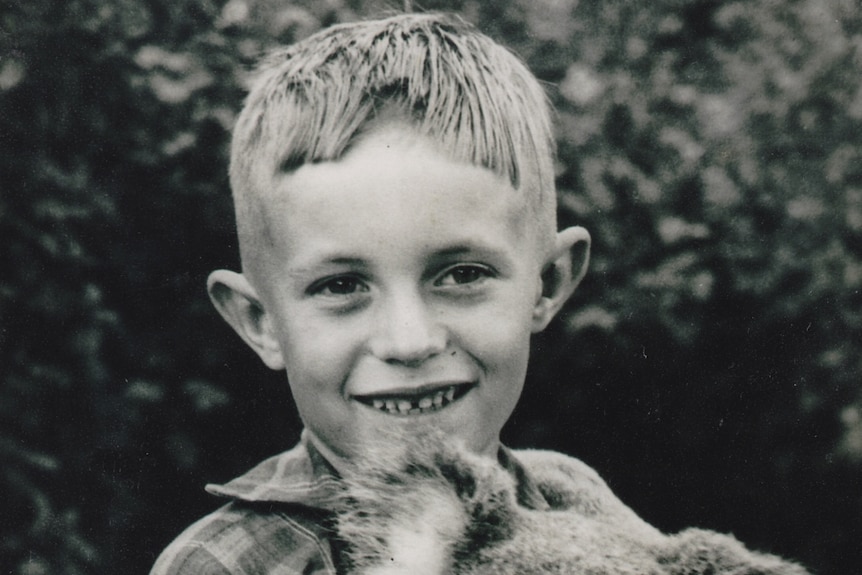 A black and white photo of a young boy holding a koala