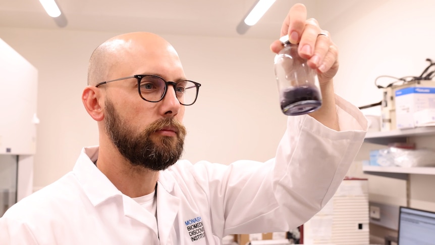 Young man holds up conical flask in a science lab