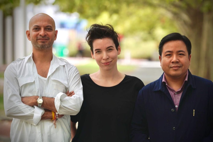 Three writers  H.M. Naqvi, Julia Phillips and Pitchaya Sudbanthad standing in front of a tree-lined street