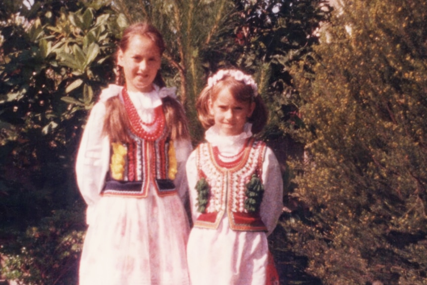 Two young girls in Polish national dress stand in front of trees 