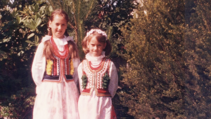 Two young girls in Polish national dress stand in front of trees.