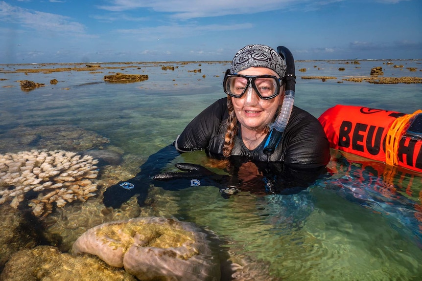 A woman in lays in shallow reef water wearing a snorkel.