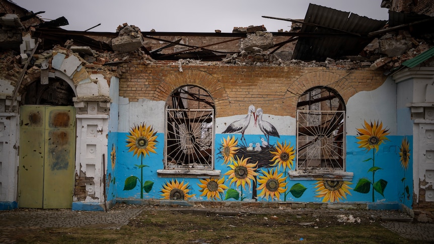 A painting of sunflowers and stalks on a heavily damaged brick building.