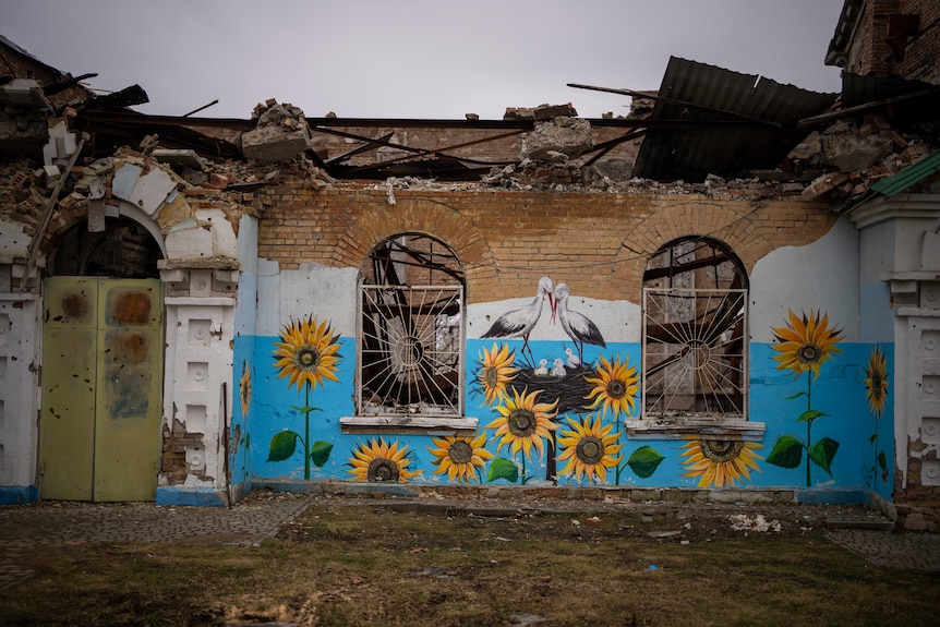 A painting of sunflowers and stalks on a heavily damaged brick building.
