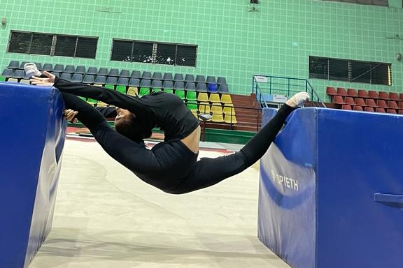 A teenage girl gymnast stretches between two blocks in a gymnasium.