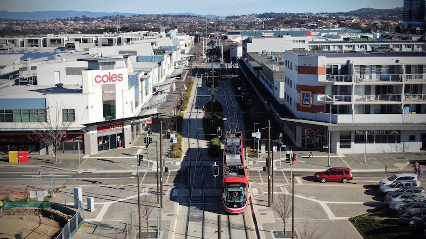 An aerial view of light rail vehicle and tracks in amongst multi-level buildings in a shopping precinct.