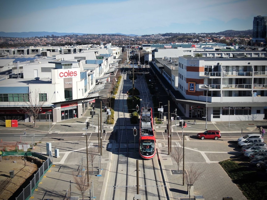 An aerial view of light rail vehicle and tracks in amongst multi-level buildings in a shopping precinct.