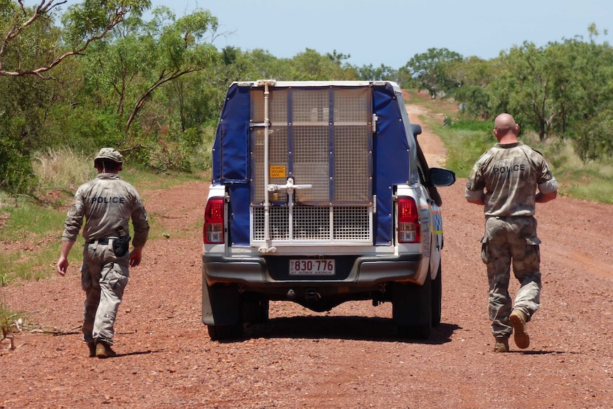 Two officers walk down the outback road with a police car between them.