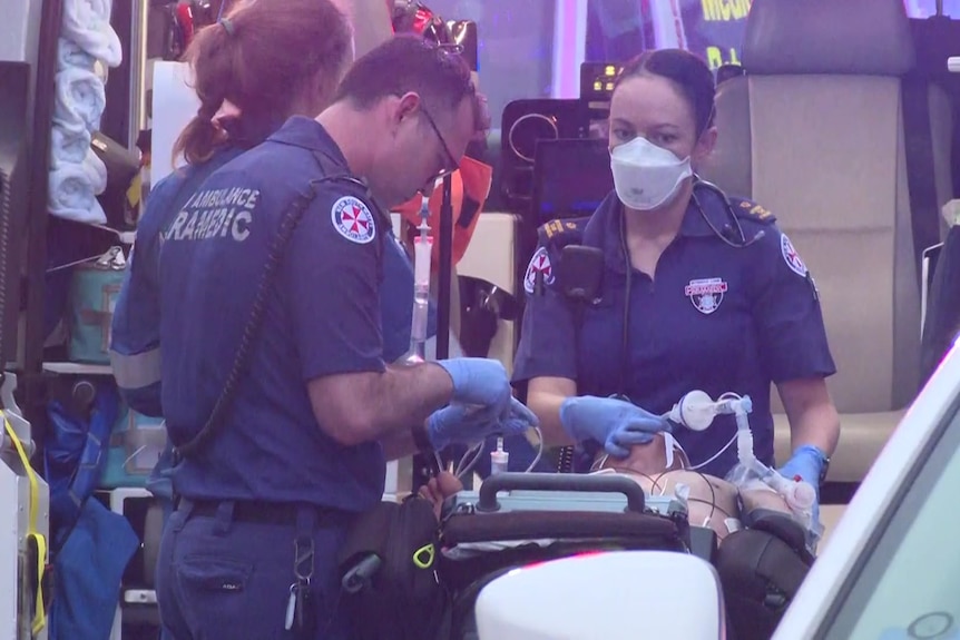 A man lies on an ambulance stretcher as two paramedics treat him