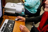 An elderly woman works on a computer.