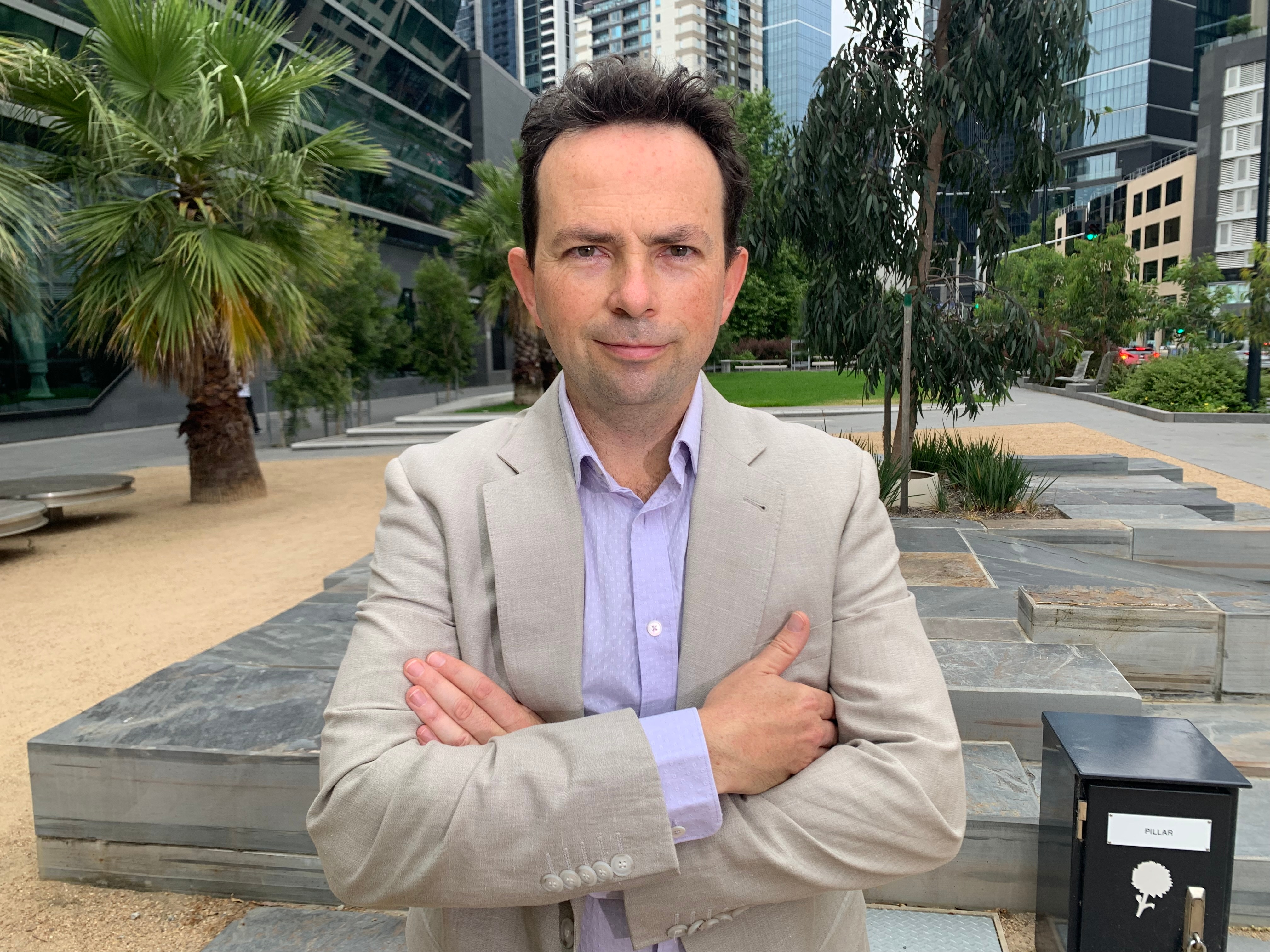 Um homem cruza os braços e olha diretamente para a câmera. 