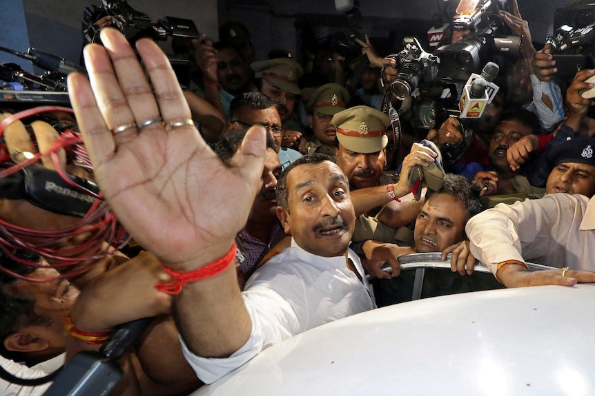 Kuldeep Singh Sengar puts his hand up and is surrounded by media and police as he tries to get into a car.