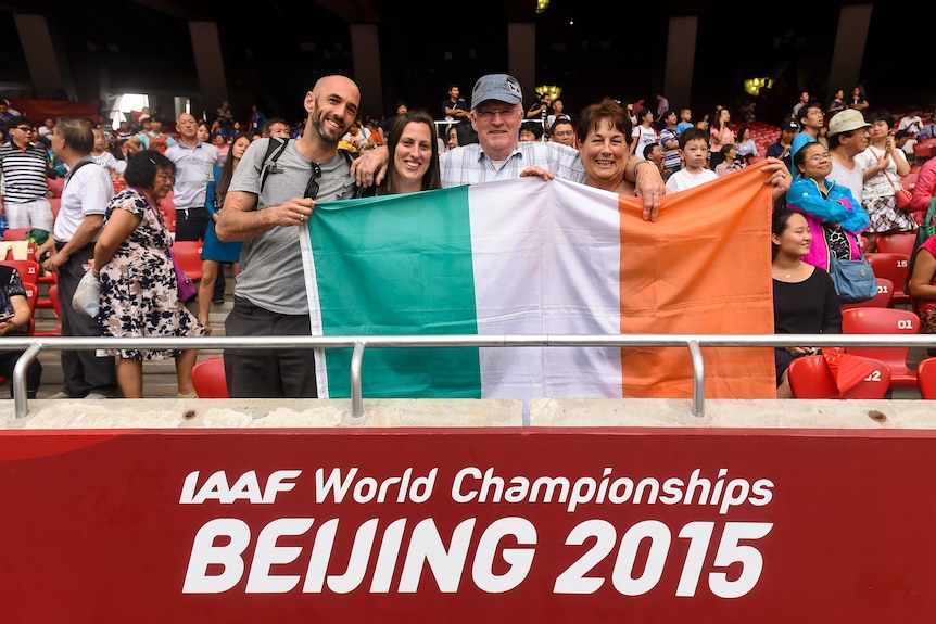 Four people smile and stand behind an Irish tricolour