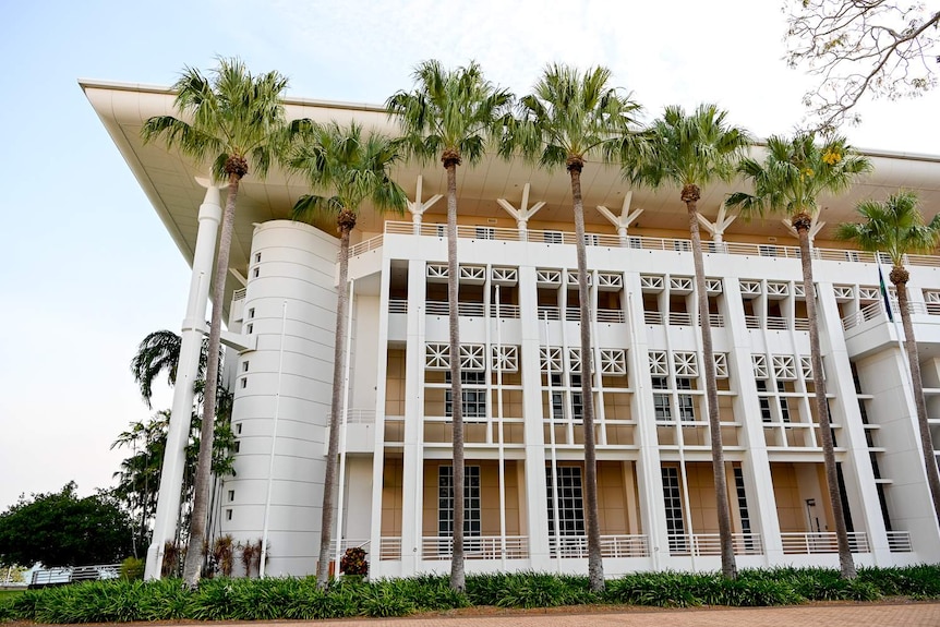 A grand looking building is surrounded by palm trees.