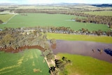 An aerial photo of brown floodwaters cutting several paths through green farm paddocks.