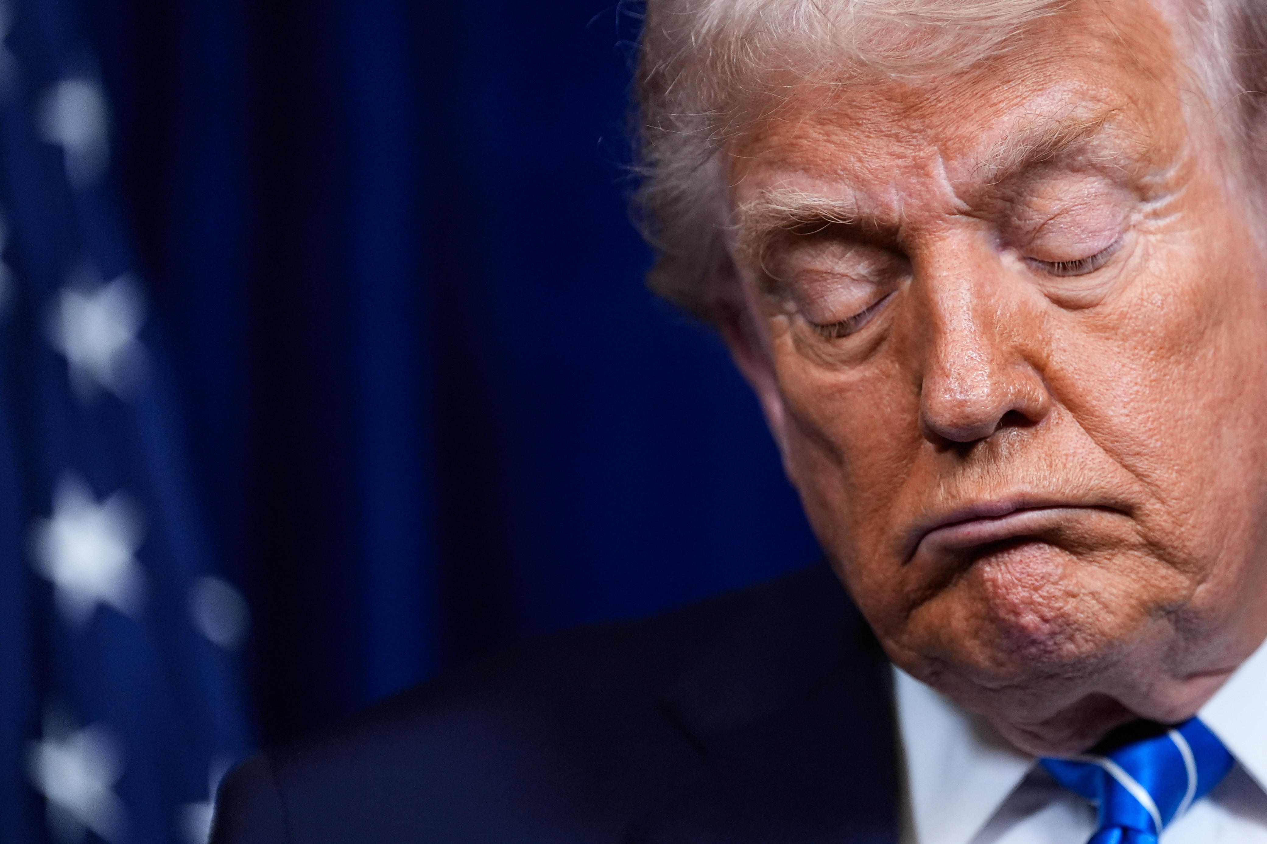 An extreme close up of Donald Trump with his eyes closed and a grimacing expression