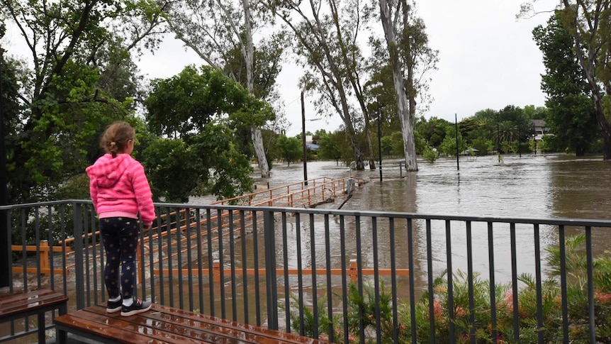 A young girl wearing a pink hoodie looks out from an overpass at rising floodwaters in the township of Euroa.