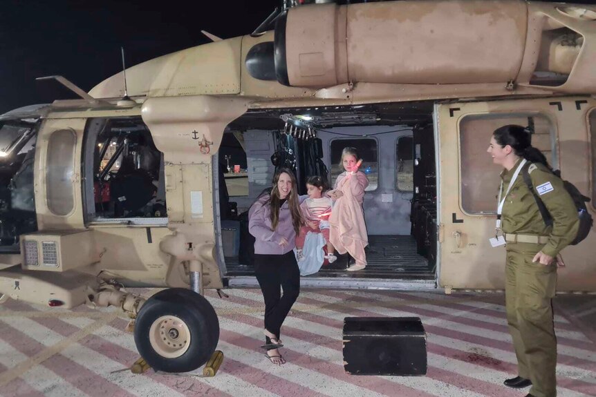 A smiling woman and two small girls at a military helicopter, with a female soldier looking on