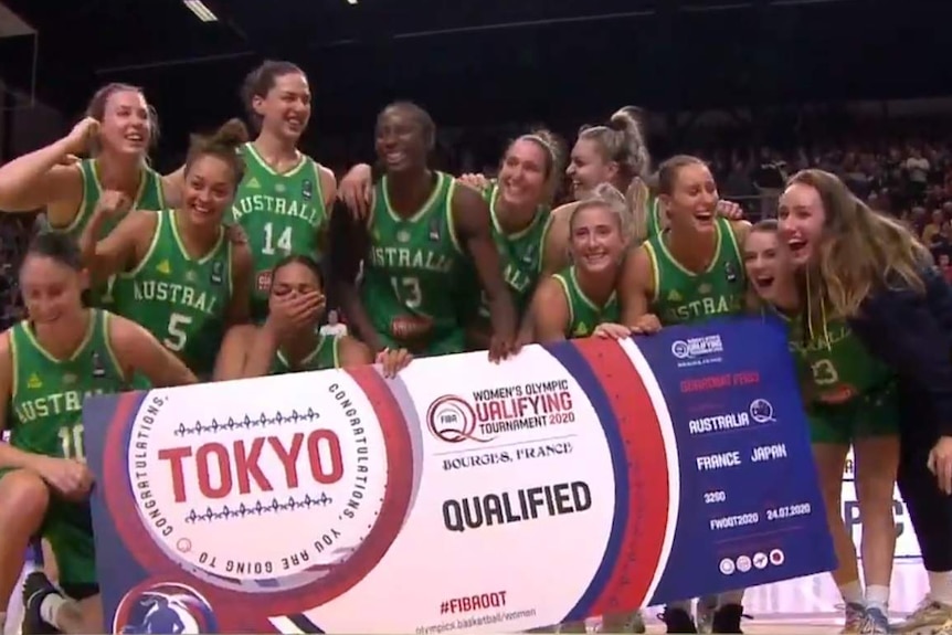 A women's basketball team celebrate holding a sign showing they have qualified for the Olympics.