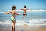 Two kids leap into the surf on a sunny day.