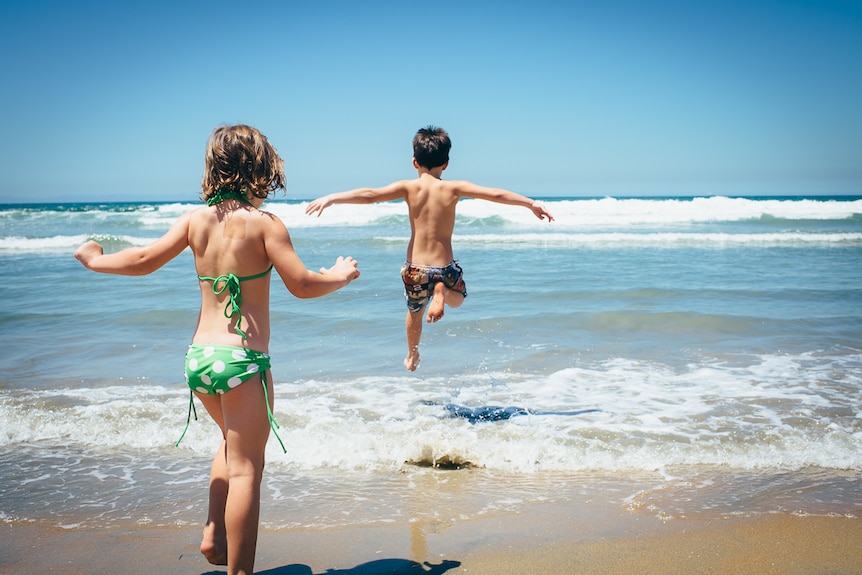 Two kids leap into the surf on a sunny day.