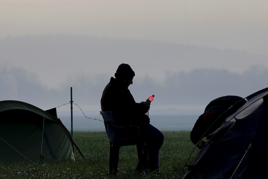 Stranded refugee sits by his tent