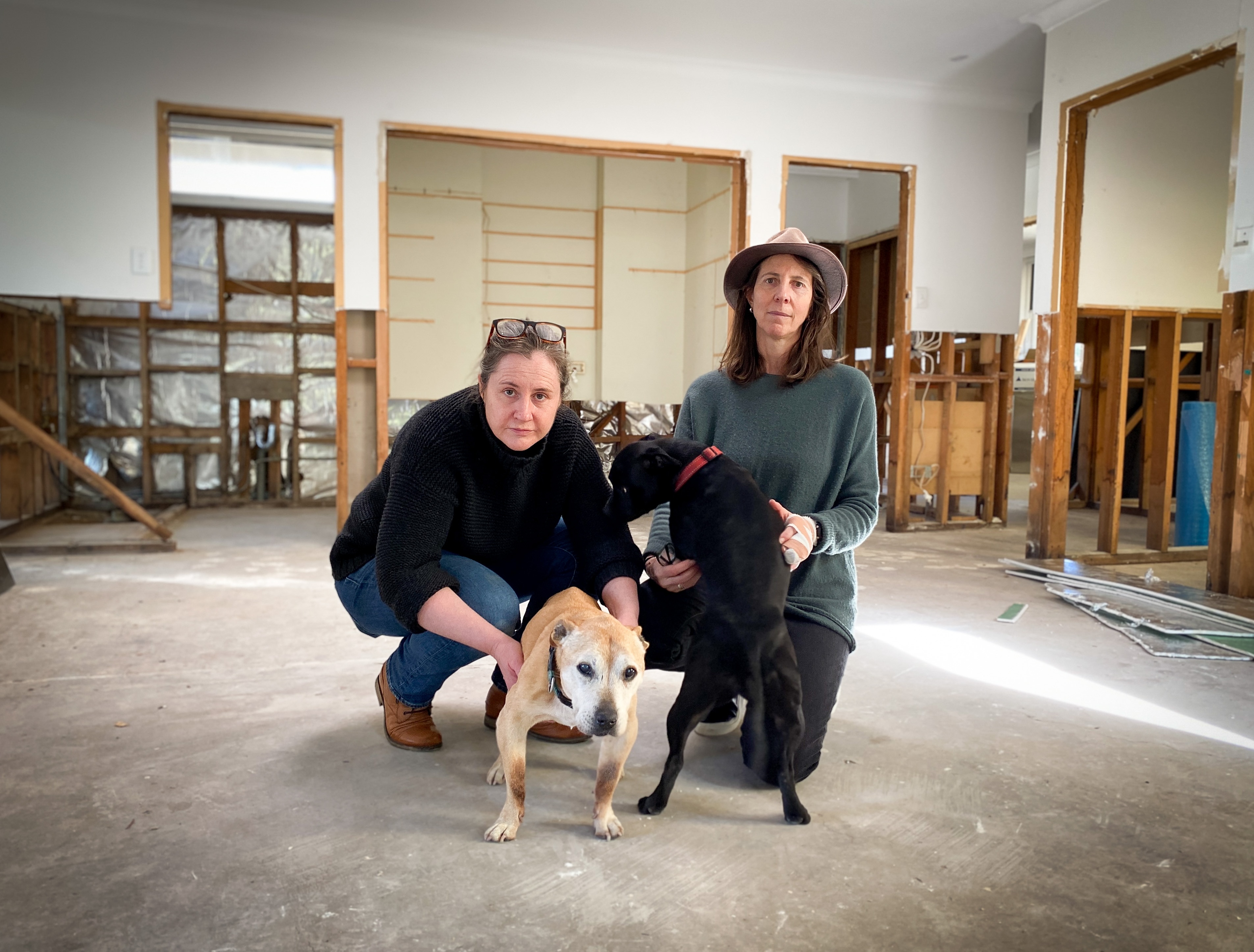 Bec Nicoll and Sarah Thomson crouch with their two dogs, on the ground of their wrecked house.