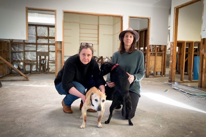 Bec Nicoll and Sarah Thomson crouch with their two dogs, on the ground of their wrecked house.