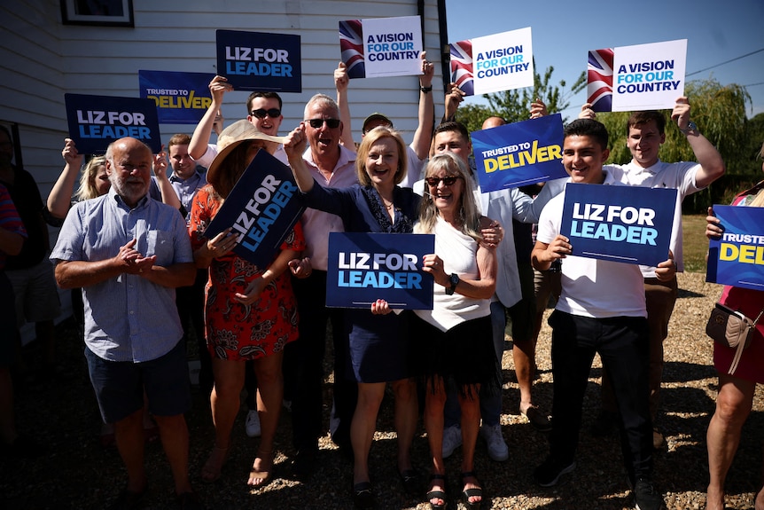 A woman stands with people who are supporting her and holding blue signs. 