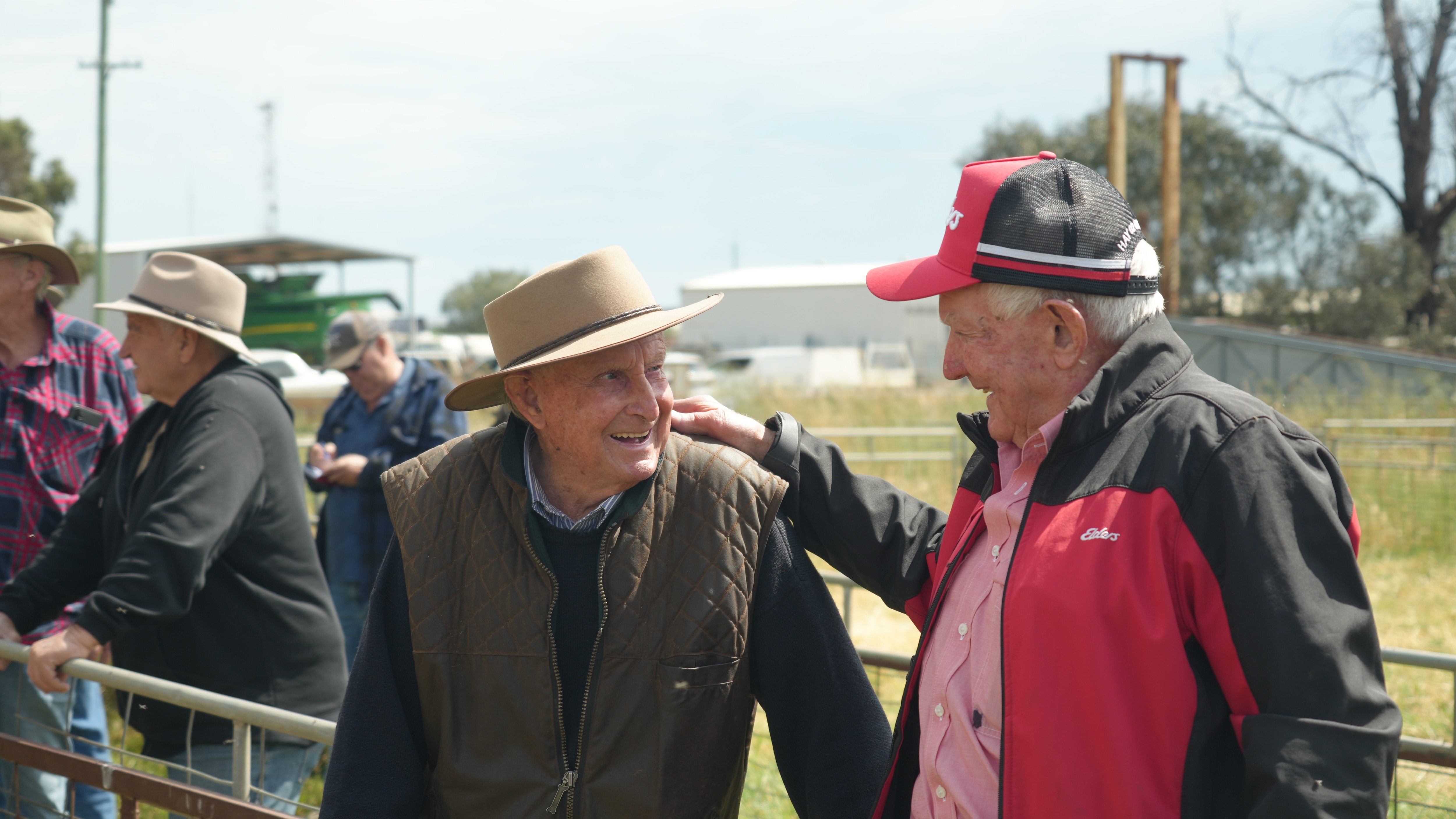 Two men smiling as they speak to each other, leaning on a rail at the saleyards