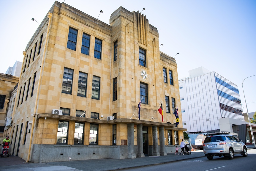 Plan large d'un bâtiment en grès de trois étages avec des drapeaux australiens et aborigènes flottant au-dessus de l'entrée.