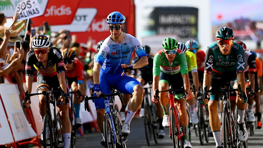 An Australian rider sits up in the saddle and reacts as he crosses the line to win a Vuelta stage in a sprint finish.