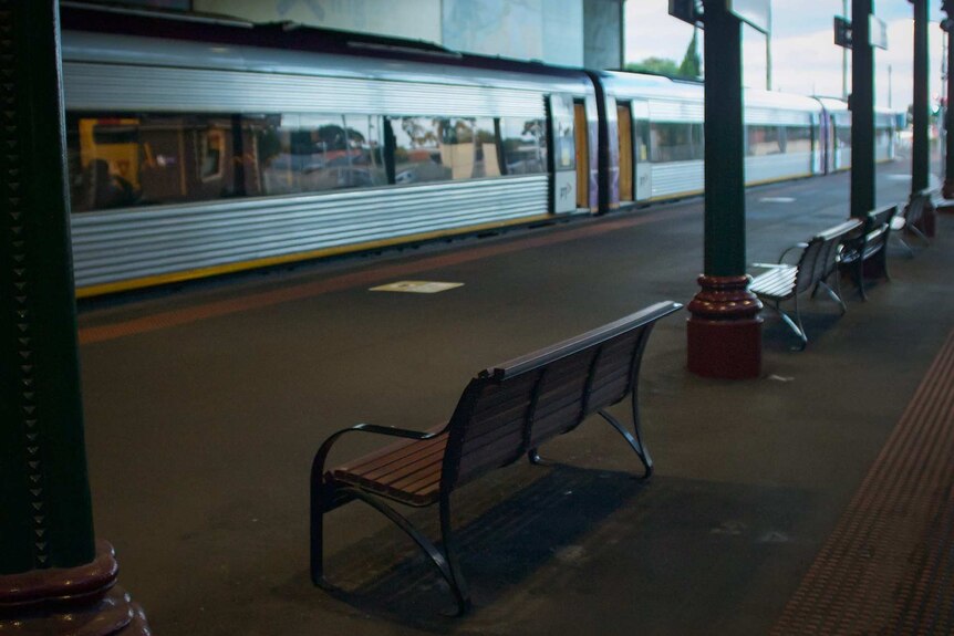 A train waits at an empty station platform with seats.