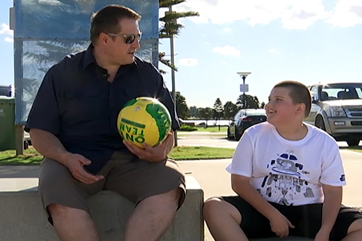 A man holding a football sitting at the beach with his son