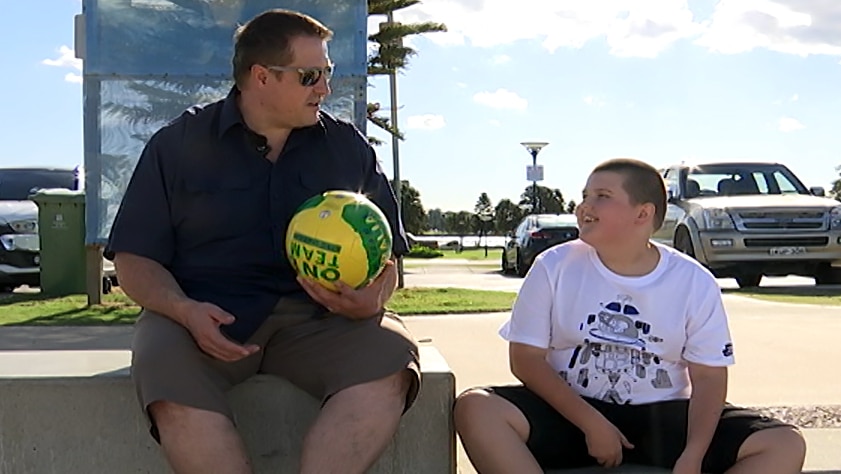 A man holding a football sitting at the beach with his son