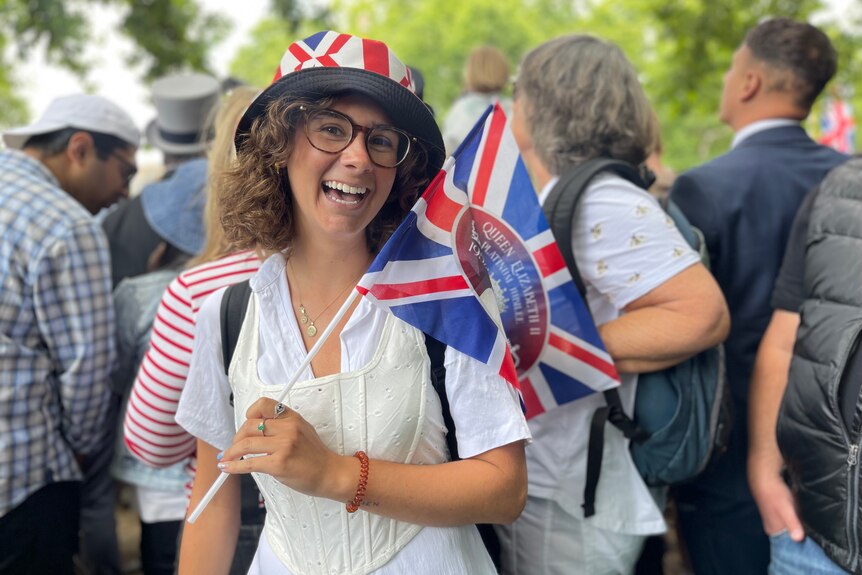 A woman with dark curly hair and glasses smiles as she waves a Union Jack flag.