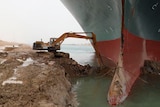 An excavator trying to dig out the keel of the large ship. 