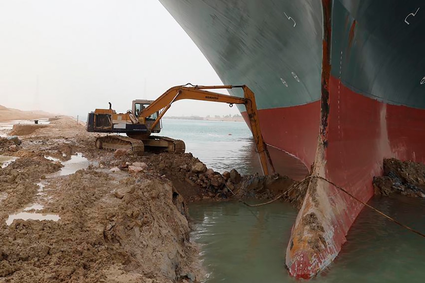An excavator trying to dig out the keel of the large ship. 