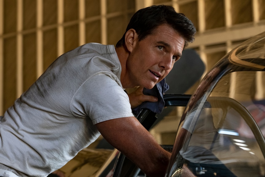 White man with cropped dark hair wears white t-shirt and leans over a car door with blue cloth in hand.