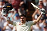 England batsman Rory Burns raises his bat and helmet into the sky in celebration.