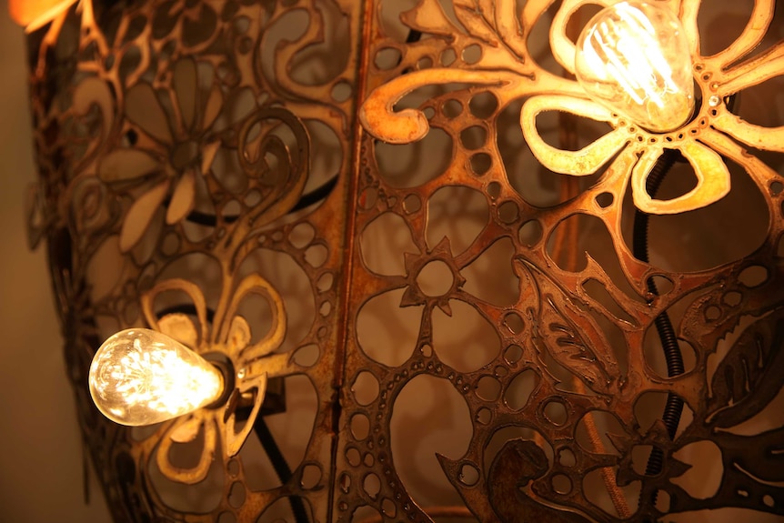 A close up on a metal sculpture featuring flower shapes cut out of a sheet of metal, illuminated with electric lightbulbs