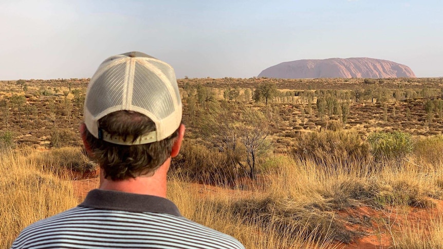 John Archer stands with his back to the camera looking towards Uluru.