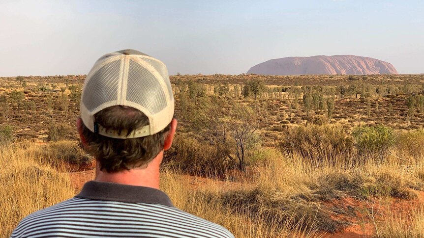 John Archer stands with his back to the camera looking towards Uluru.