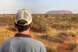 John Archer stands with his back to the camera looking towards Uluru.