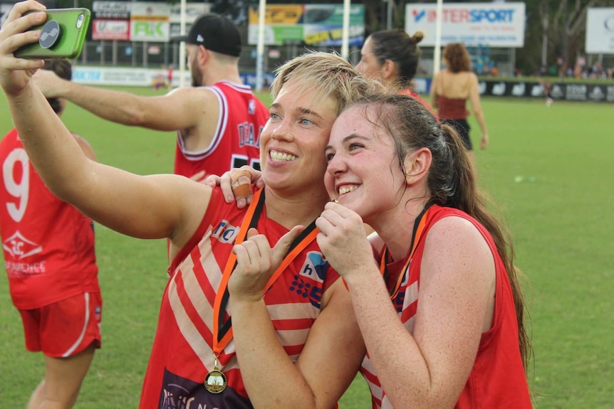 Two women's football players take a selfie on the football field.